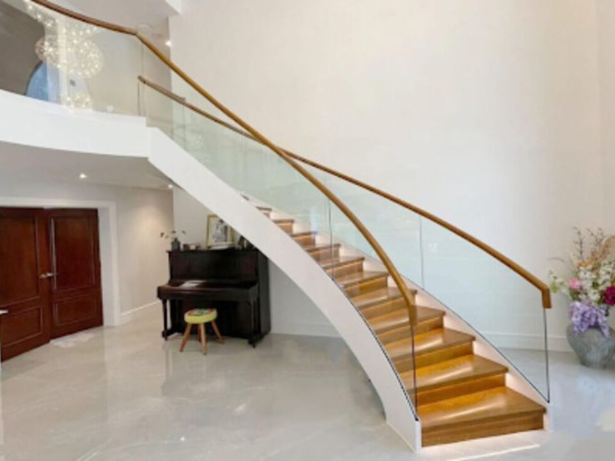 Cầu thang uốn cong uyển chuyển với lan can k&iacute;nh v&agrave; tay nắm gỗ tự nhi&ecirc;n